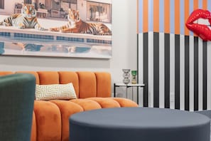 Een moderne woonkamer met een bank, een rond voetenbankje, een schilderij van een tijger, en een gestreepte muur met een rode lippen decoratie.