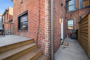 A brick building with a wooden deck, a window, and a grill area. - Modern Palm Springs Retreat| 4 BR 4 Bath| Central (Pittsburgh)