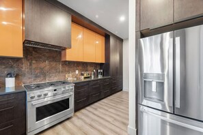 A modern kitchen with a stainless steel stove, oven, and refrigerator, dark wooden cabinets, and a marble backsplash. - Modern Palm Springs Retreat| 4 BR 4 Bath| Central (Pittsburgh)