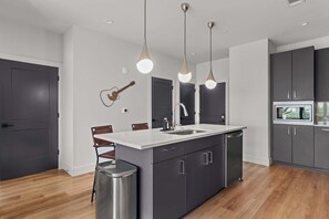 A modern kitchen with a central island, dark cabinetry, and pendant lighting. - The Rhiannon | Pool, Parking & Private Balcony (Nashville)