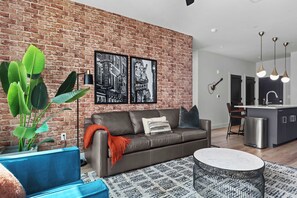 A modern living room with a brick wall, a sofa, a coffee table, and a plant. - The Rhiannon | Pool, Parking & Private Balcony (Nashville)