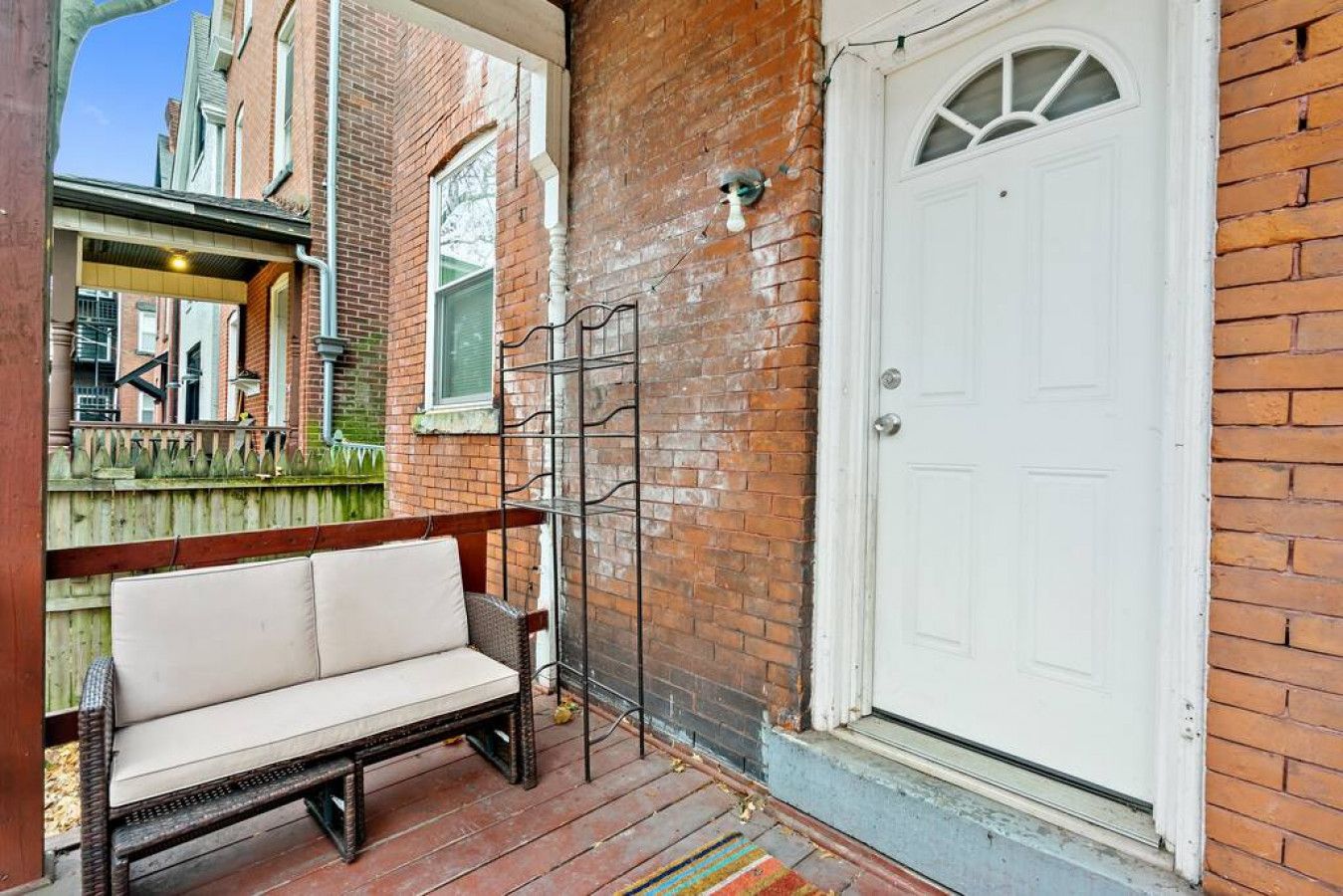 A brick exterior with a white door, a wooden bench, and a metal gate.