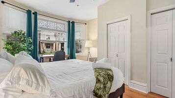 A hotel room with a bed, a desk, a chair, a lamp, and a view of the outside.