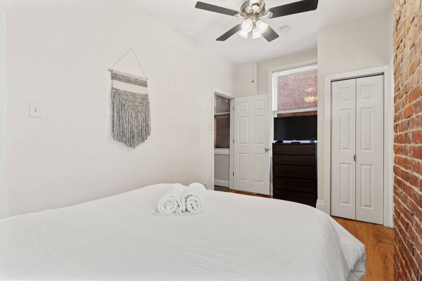 A bedroom with a bed, a ceiling fan, a door, and a wall-mounted light fixture.