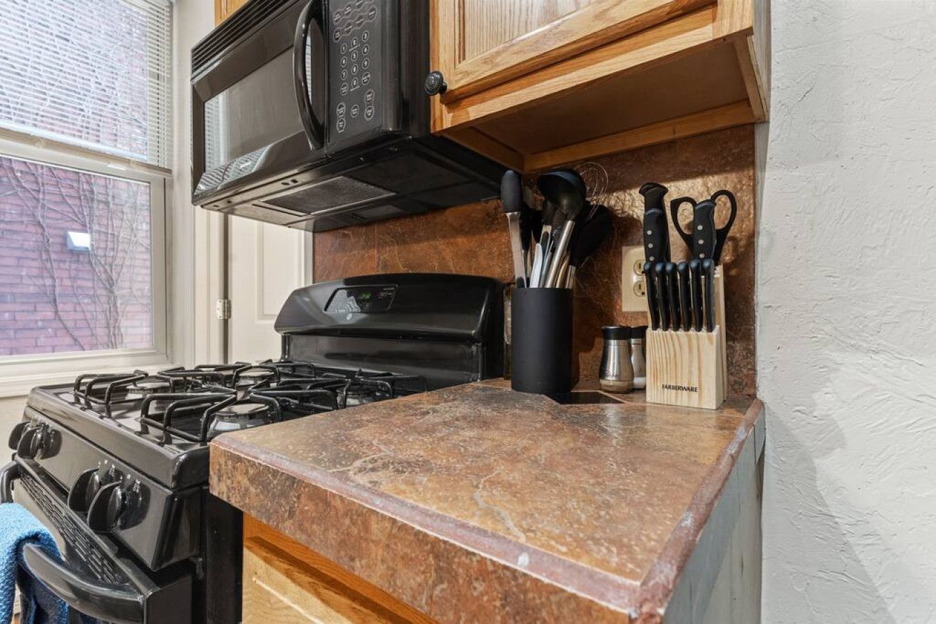 A kitchen with a gas stove, a microwave, and a knife block on the countertop.