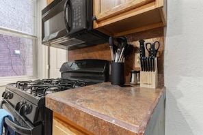 A kitchen with a gas stove, a microwave, and a knife block on the countertop. - 5531 Kentucky APT 1 · Cozy 2BR ~ $0 cleaning fee & steps from Walnut St! (Pittsburgh)