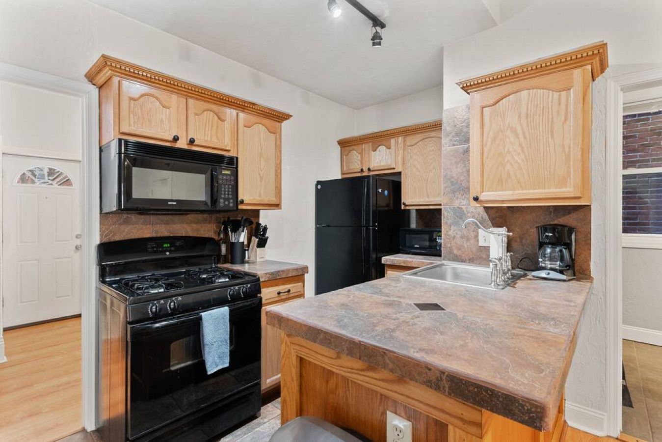 A kitchen with wooden cabinets, a black stove, a microwave, a refrigerator, and a granite countertop.