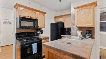 A kitchen with wooden cabinets, a black stove, a microwave, a refrigerator, and a granite countertop.