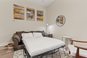 A bedroom with a bed, a sofa, a round mirror, and artwork on the wall. - 615 Summerlea APT 2 · Free Off-Street Parking~Super safe & walkable! (Pittsburgh)