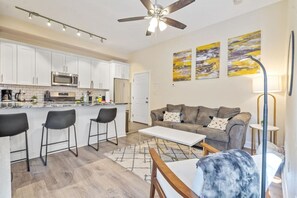 A modern kitchen with white cabinets, a central island with bar stools, a grey sofa with patterned cushions, and a ceiling fan. - 615 Summerlea APT 2 · Free Off-Street Parking~Super safe & walkable! (Pittsburgh)