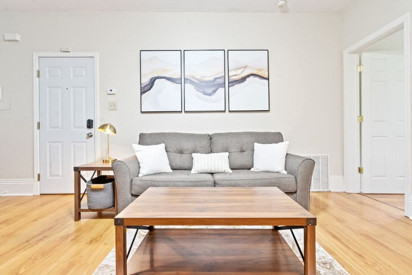 A living room with a grey sofa, a wooden coffee table, and three abstract paintings on the wall.