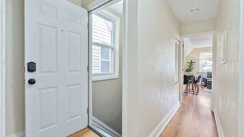 A hallway with a white door, a window, and a view into a dining area with a table and chairs.