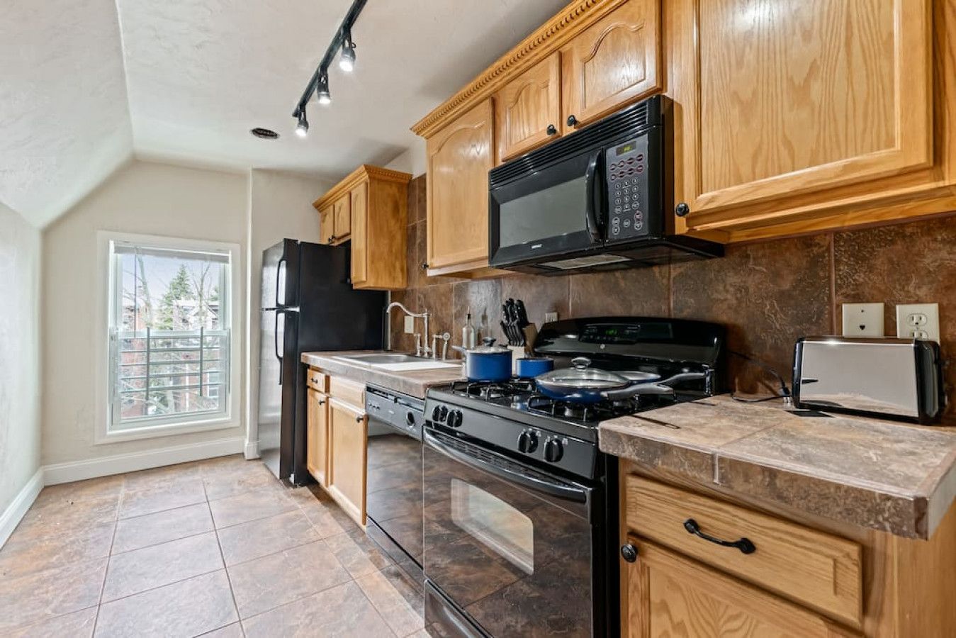 A kitchen with wooden cabinets, a black microwave, a stove, and a toaster.
