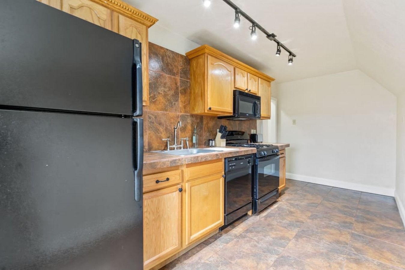 A kitchen with wooden cabinets, a black refrigerator, a microwave, a stove, and a dishwasher.