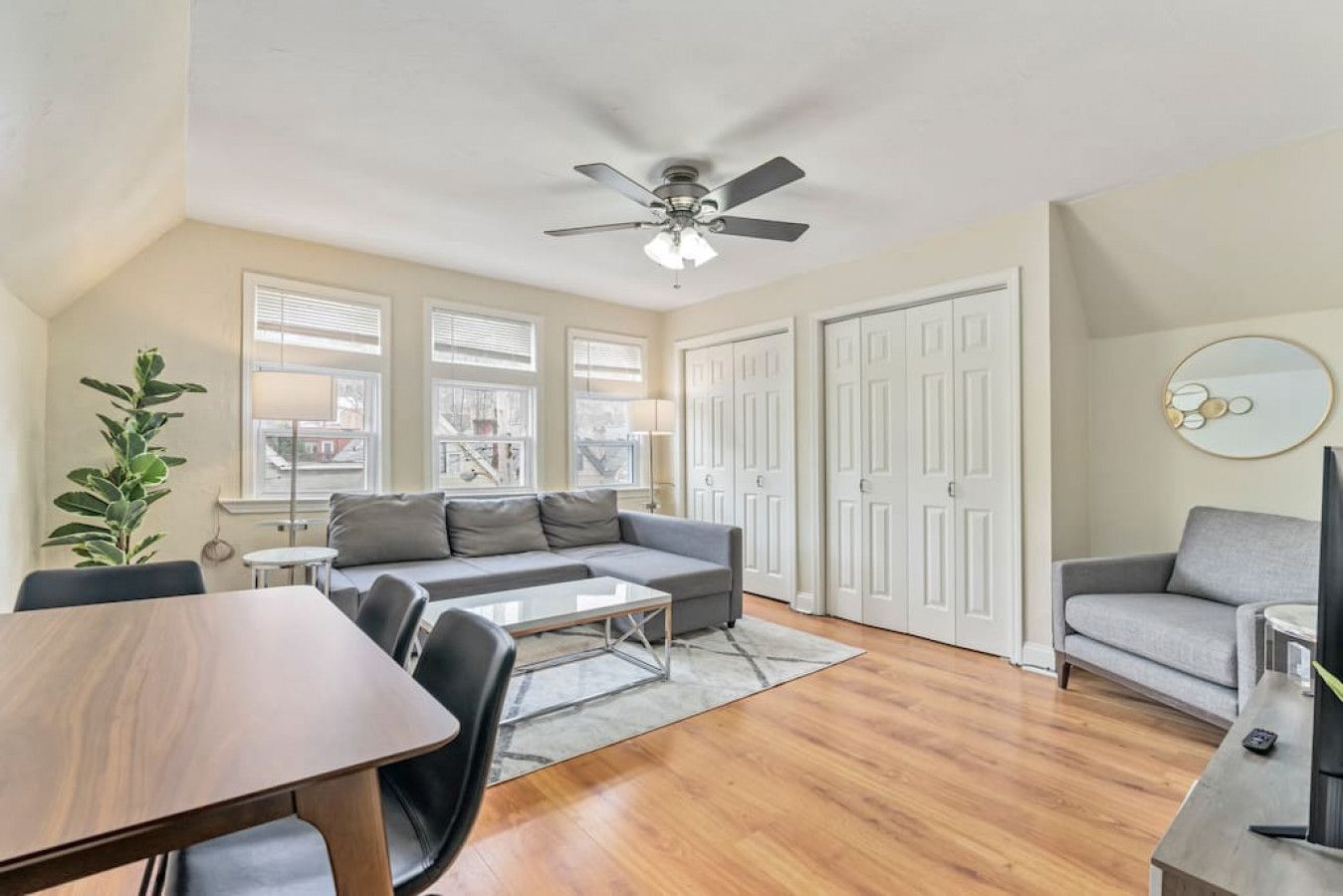 A modern living room with a sofa, a dining table, and a ceiling fan.