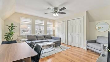 A modern living room with a sofa, a dining table, and a ceiling fan.