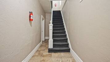 A hallway with a carpeted staircase, a fire extinguisher mounted on the wall, and a door at the end.