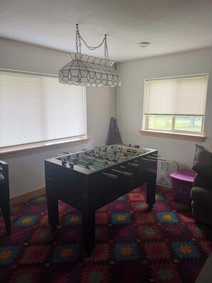 A room with a foosball table, a hanging light fixture, and a window with blinds. - Star Lake Escape, Dent MN (Dent)