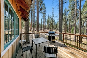 Eine Holzterrasse mit Tisch, Stühlen, einem Grill und Blick auf einen Wald.