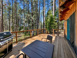A deck with a grill, a table, and chairs, surrounded by a forest. - The Forest Haus: Hot Tub, Pets, Hiking, BBQ (South Lake Tahoe)