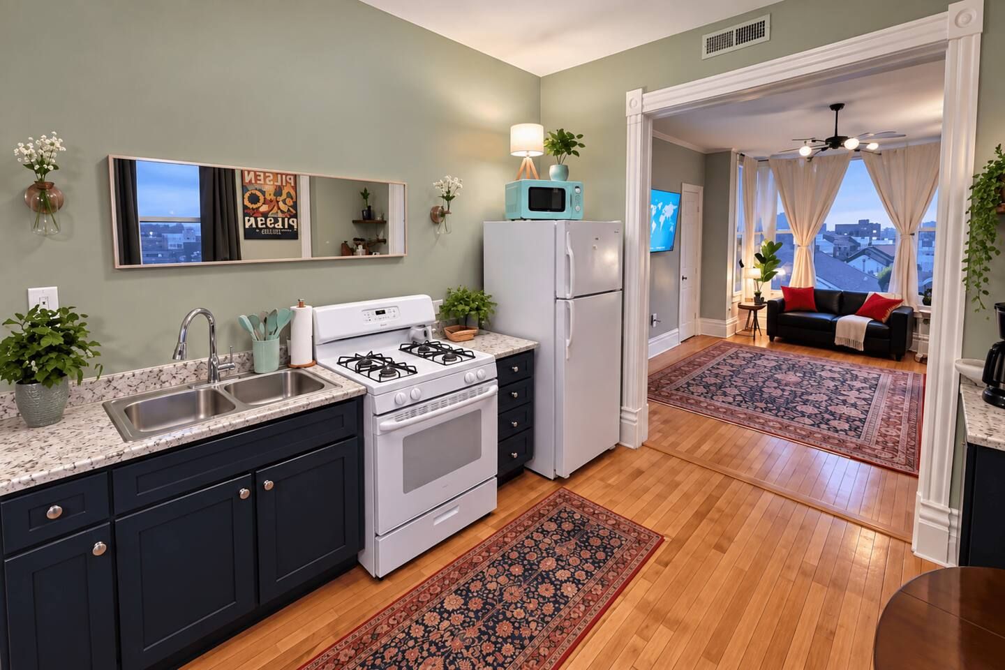 Eine moderne Küche mit Herd, Spüle und Kühlschrank, angrenzend an einen Wohnbereich mit einer Couch und Blick auf die Stadt.