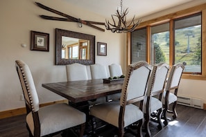A dining room with a wooden table and six upholstered chairs, a chandelier, and a large mirror on the wall. - AN122 | Newly Listed | Winter Shuttle | Ski In/Out (Steamboat Springs)