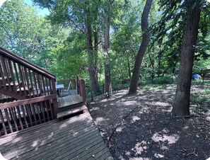 A wooden deck leading into a wooded area with a bench and a picnic table. - Falcon Forest Retreat: Near Offutt AFB & Omaha Zoo (Bellevue)