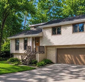 A two-story house with a front garage, a front porch with a staircase, and a brick foundation. - Falcon Forest Retreat: Near Offutt AFB & Omaha Zoo (Bellevue)