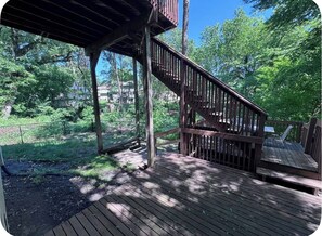 A wooden deck with a staircase leading to a covered area, surrounded by greenery. - Falcon Forest Retreat: Near Offutt AFB & Omaha Zoo (Bellevue)