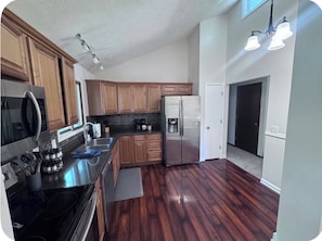 A kitchen with wooden cabinets, stainless steel appliances, and a dark wood floor. - Falcon Forest Retreat: Near Offutt AFB & Omaha Zoo (Bellevue)