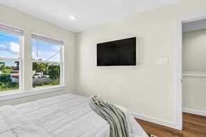 Ein Schlafzimmer mit einem Bett, einem Flachbildfernseher an der Wand und einem Fenster mit Blick ins Freie.