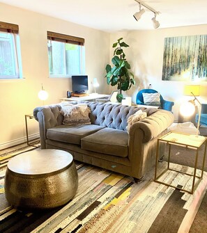 A living room with a sofa, a coffee table, a lamp, a plant, and a painting on the wall. - Spacious Two Bedroom, WD in Unit Fireplace, Pet Friendly, Near Shopping (Shoreline)