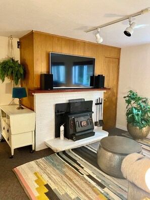 Ein Wohnzimmer mit Kamin, einem darüber hängenden Fernseher und einer Zimmerpflanze zur Rechten.