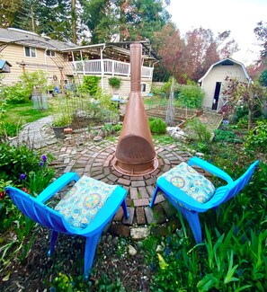 Eine Terrasse mit einem zentralen Feuerkorb, umgeben von zwei blauen Sesseln mit gemusterten Kissen.