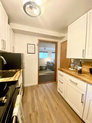 A narrow kitchen with white cabinets, a wooden countertop, and a view into a living room through an open doorway. - Spacious Two Bedroom, WD in Unit Fireplace, Pet Friendly, Near Shopping (Shoreline)