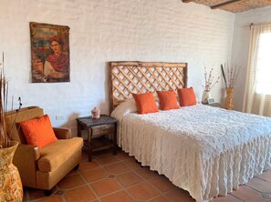 A bedroom with a bed, a chair, a nightstand, a painting on the wall, and a window with curtains. - Villa Isabela +10 Guests | Pool | Huge Garden (San Miguel Cuyutlán)