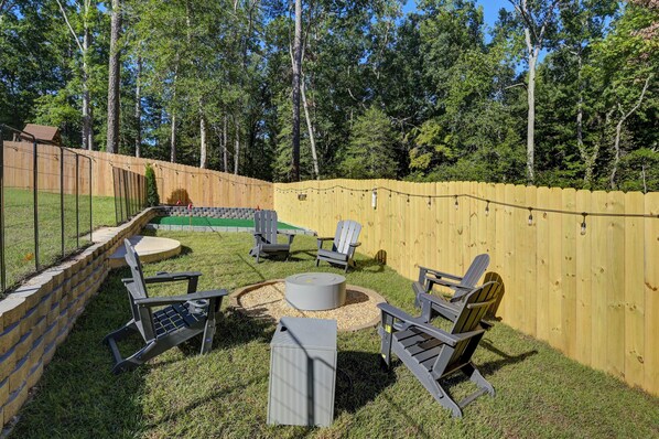 A backyard with a wooden fence, a fire pit, and outdoor seating.