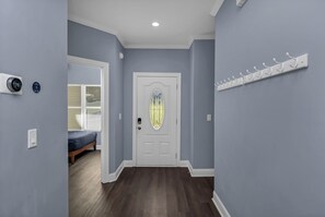 A hallway with a white door, a coat rack, and a thermostat on the wall.