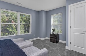 A bedroom with a bed, a dresser, and two windows with blinds.
