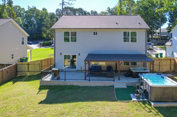 A two-story house with a covered patio, a hot tub, and a fenced yard.