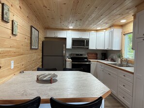 Une cuisine avec des murs en bois, des armoires blanches, un réfrigérateur en acier inoxydable, un four à micro-ondes, une cuisinière et un évier.