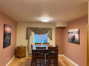 Une salle à manger avec une table et des chaises, une fenêtre avec des rideaux et des œuvres d’art accrochées aux murs.