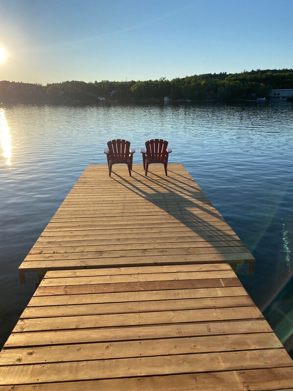A wooden dock extending into calm water with two Adirondack chairs facing the water.
