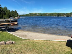 A lakeside dock with boats, a grassy area, and a view of hills in the distance. - Waterfront 4BR Home on the beach. Parking. Wifi. Long Lake. (Greater Sudbury)