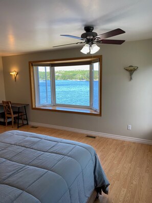 Une chambre avec un grand lit, un ventilateur de plafond, une fenêtre donnant sur l’eau et un bureau avec une chaise.
