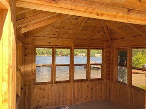 A cabin with a wooden interior, large windows overlooking a lake, and a visible dock.