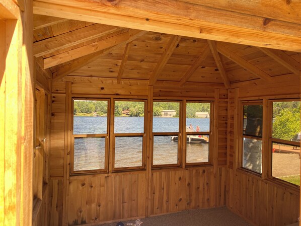 Une cabane avec un intérieur en bois, de grandes fenêtres donnant sur un lac et une jetée visible.