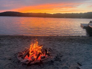 A beach with a campfire and a dock extending into calm waters.
