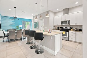 A modern kitchen with white cabinets, a central island with bar stools, stainless steel appliances, and pendant lighting. - 12 Min to Disney, Mickey & Minions Themed Rooms (Kissimmee)
