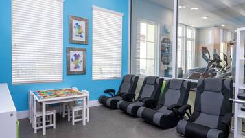 Ein Zimmer mit blauer Wand, weißen Jalousien, einem Kindertisch mit bunten Brettspielen und Trainingsgeräten.